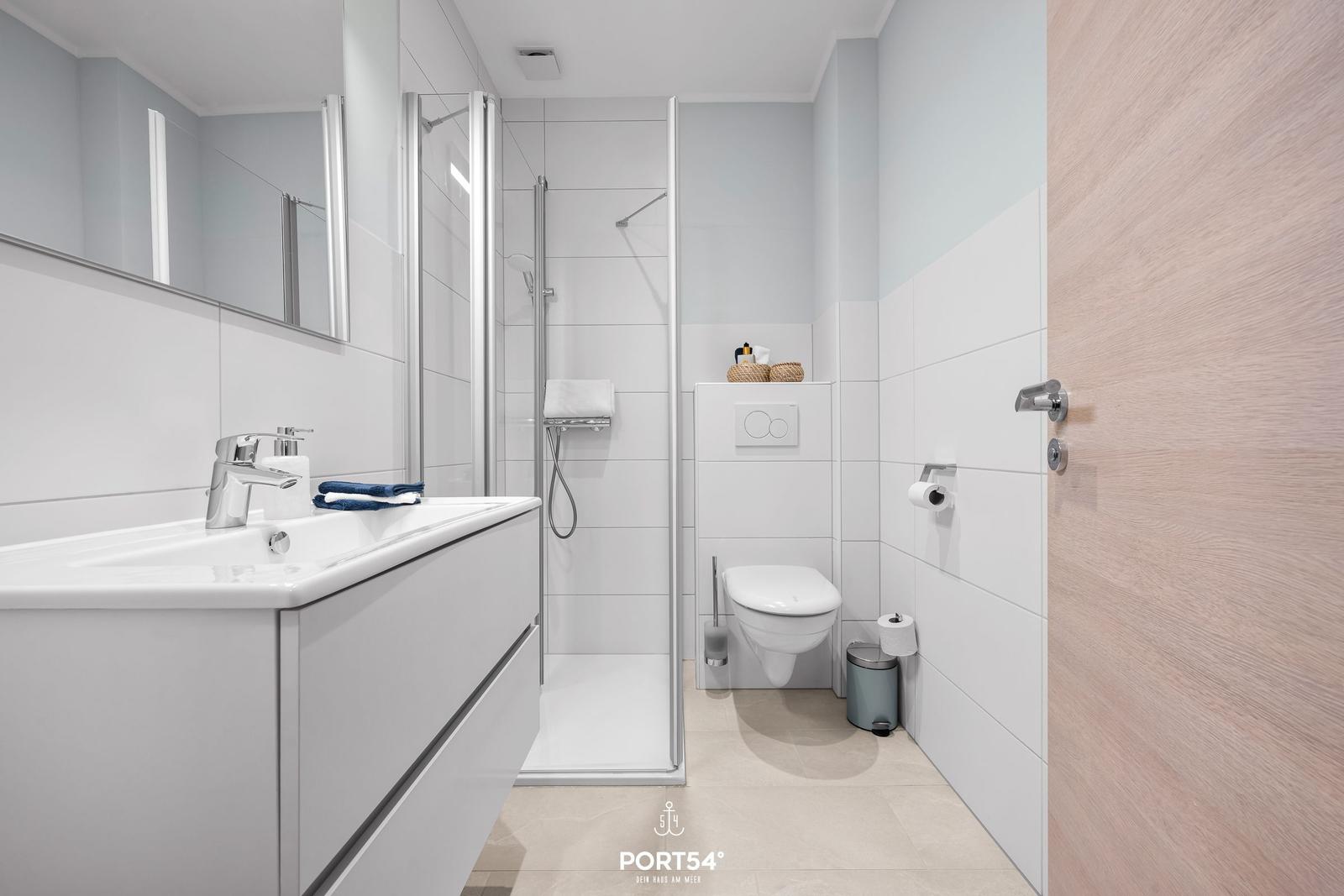 Badezimmer mit Dusche, Waschbecken und Toilette. Moderne Einrichtung mit hellen Fliesen.