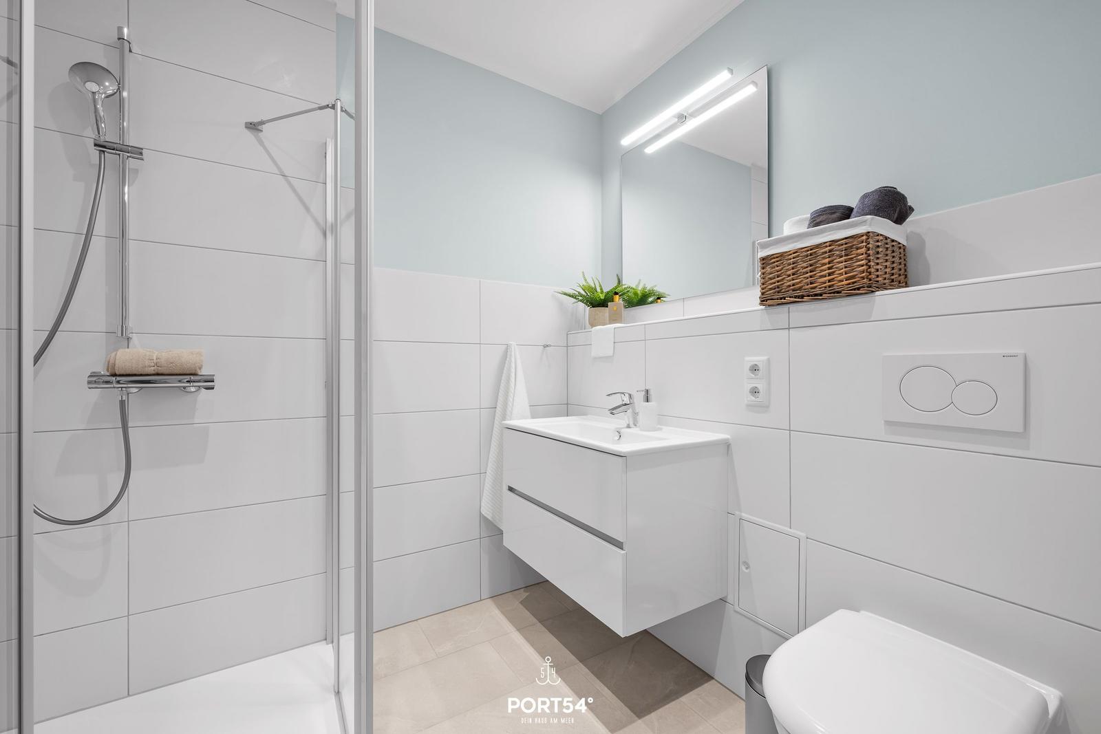 Moderne Badezimmer mit Dusche, Waschbecken und Toilette. Weiße Fliesen und Spiegelschrank.