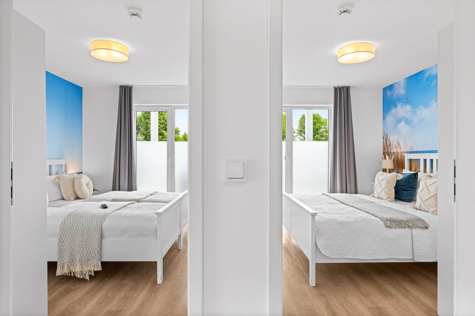 Zwei Schlafzimmer mit weißen Betten und blauen Wandbildern. Holzboden und Fenster mit Vorhängen.