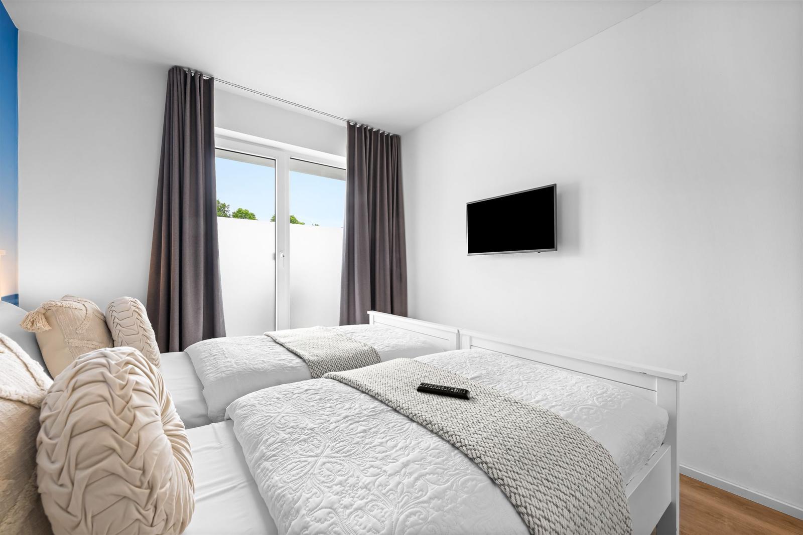 Schlafzimmer mit Doppelbett, TV und Fenster mit Blick auf Außenbereich.