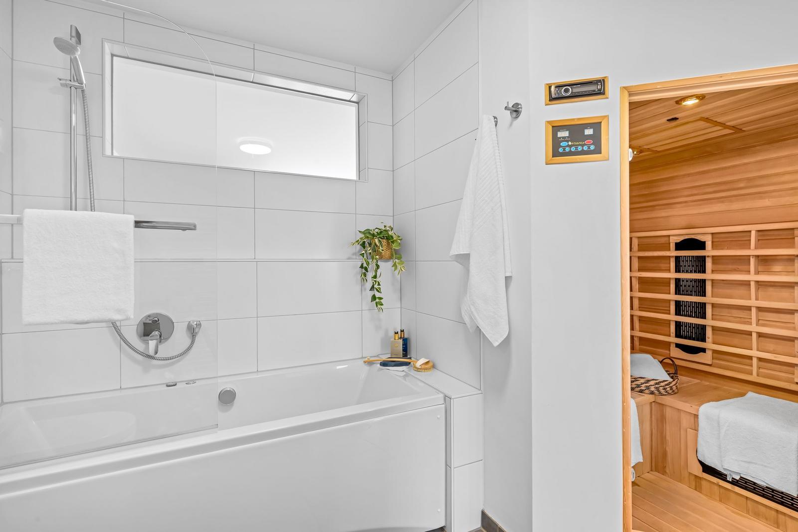 Badezimmer mit Badewanne und Dusche. Nebenraum ist eine Sauna mit Holzverkleidung.