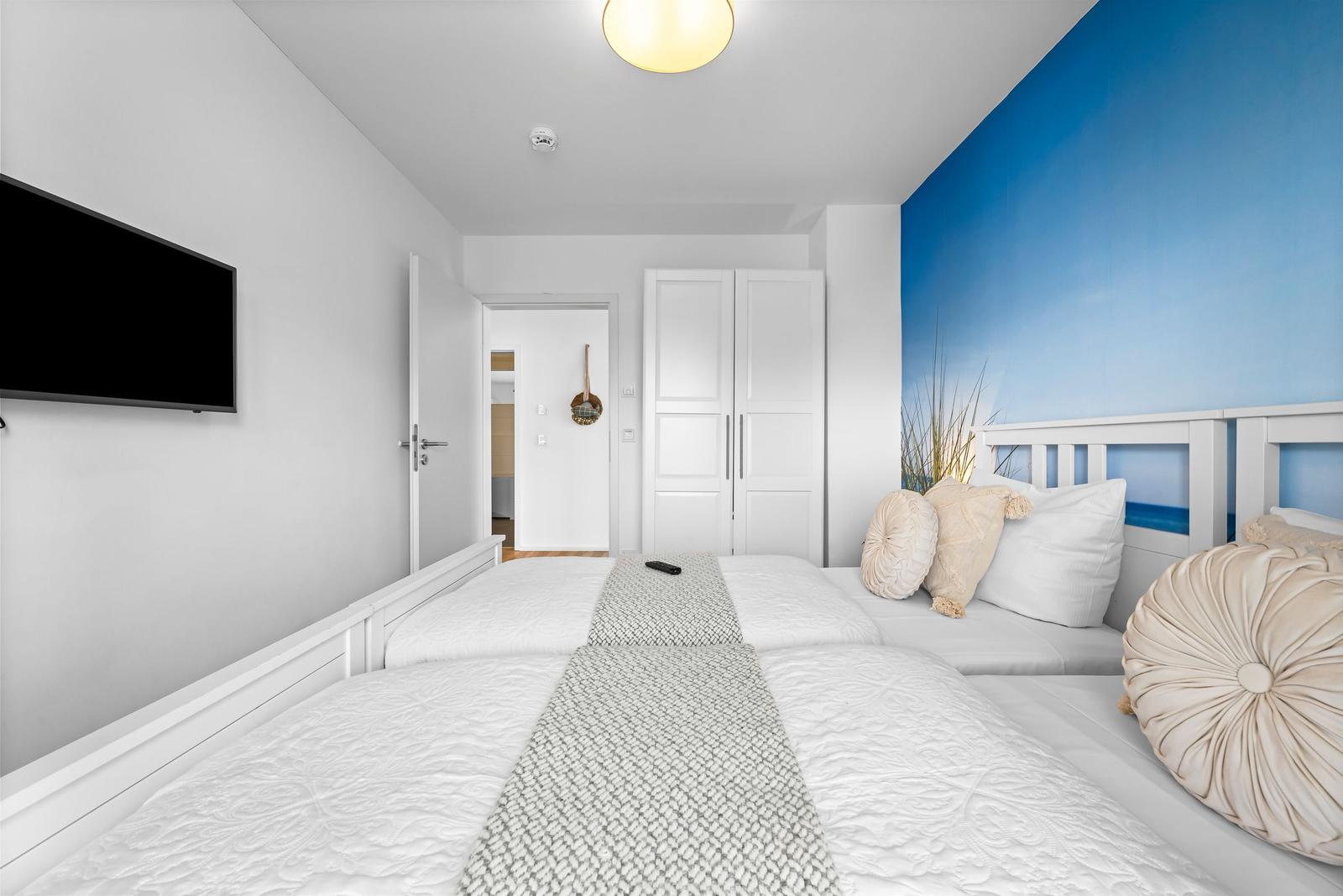 Schlafzimmer mit weißem Bett, blauer Wand und Fernseher an der Wand.