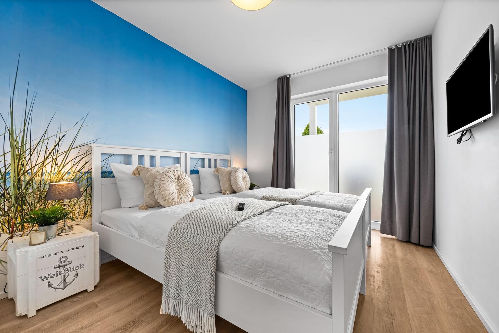 Schlafzimmer mit Doppelbett, blauer Wand und Balkonansicht.