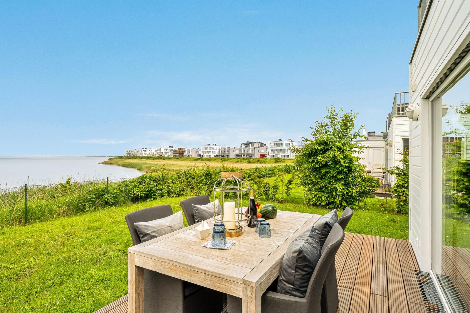 Terrasse mit Tisch und Stühlen. Blick auf Wasser und Grünflächen.