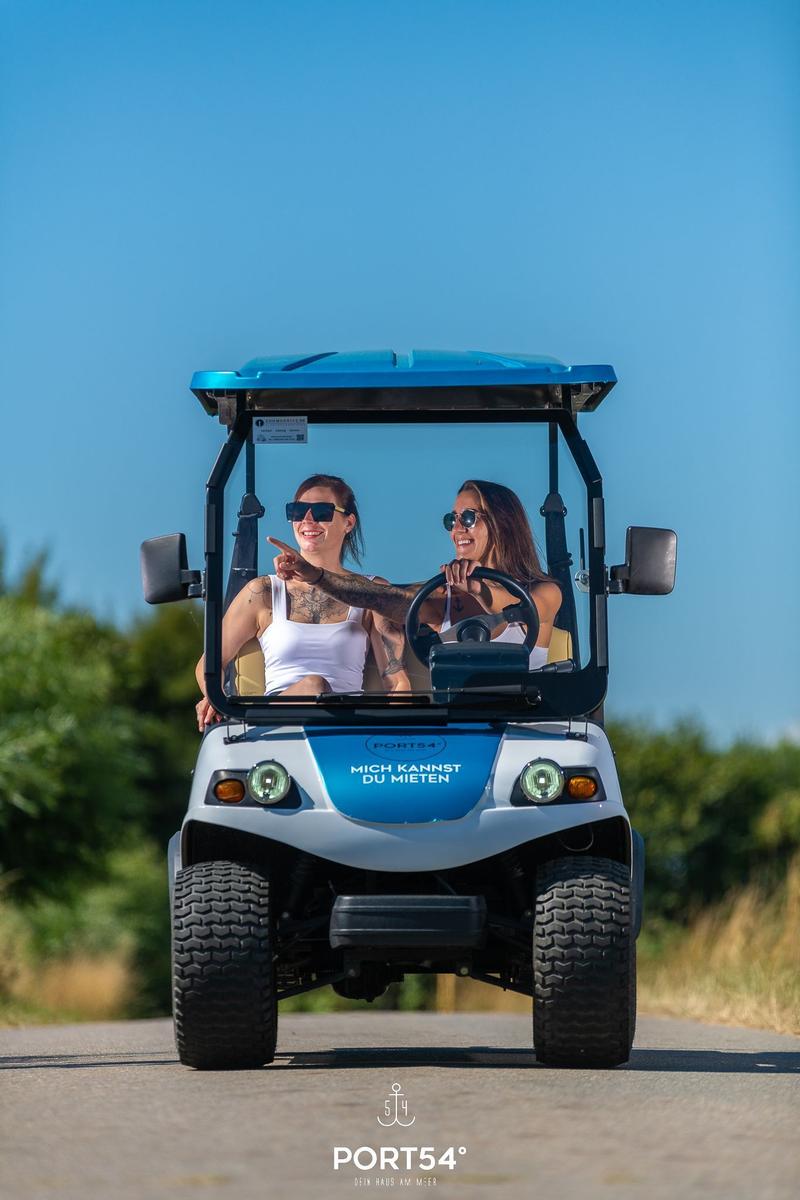 Zwei Frauen fahren in einem blauen Golfcart auf einer Straße.