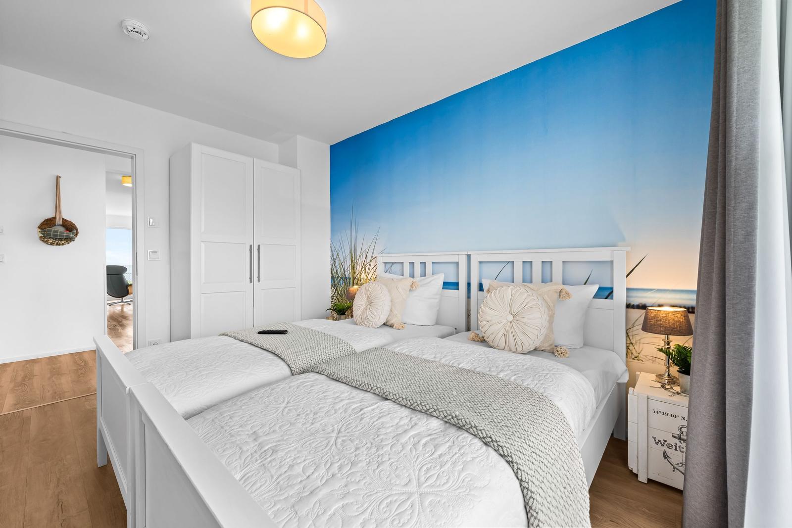 Schlafzimmer mit weißem Bett, blauer Wand und Holzboden.