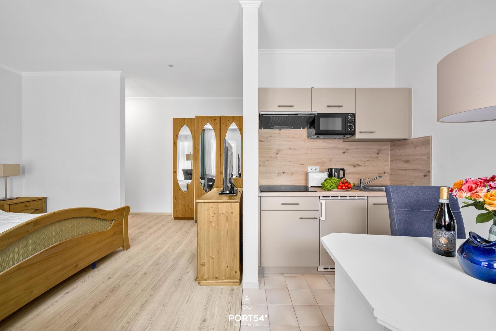 Schlafzimmer mit Bett und Küchenbereich mit Arbeitsplatte und Geräten.