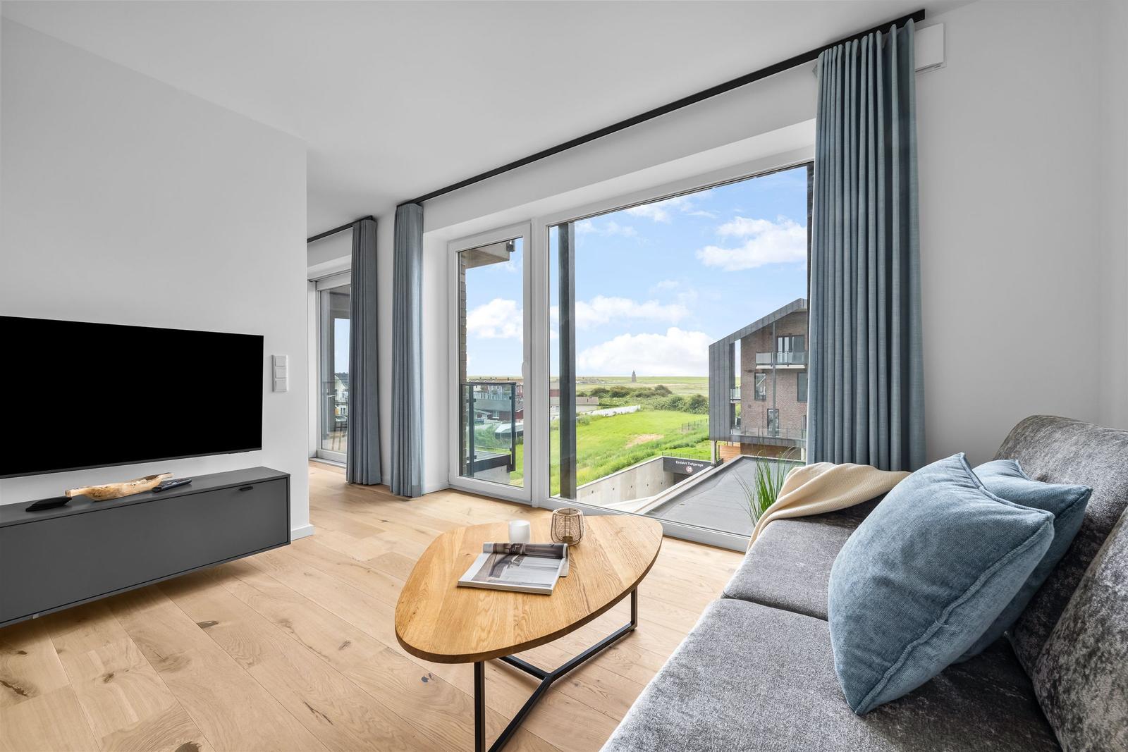 Wohnzimmer mit Sofa, TV und großem Fenster mit Blick auf Grünfläche.