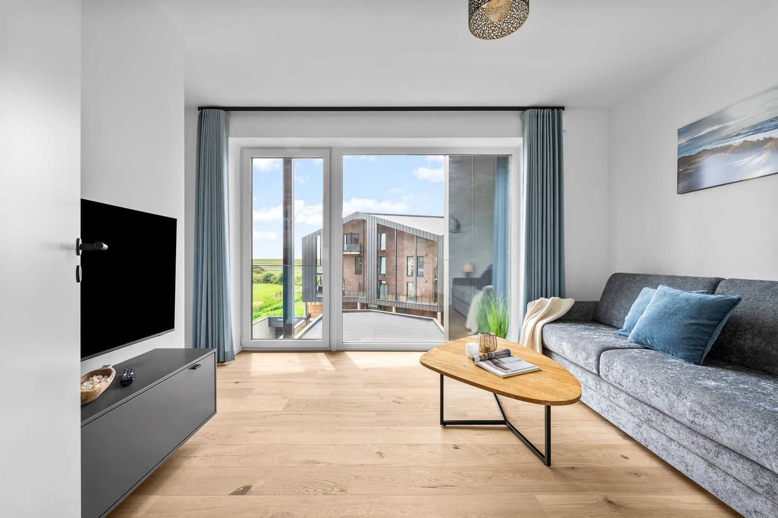 Wohnzimmer mit Sofa, TV und Blick auf Balkon