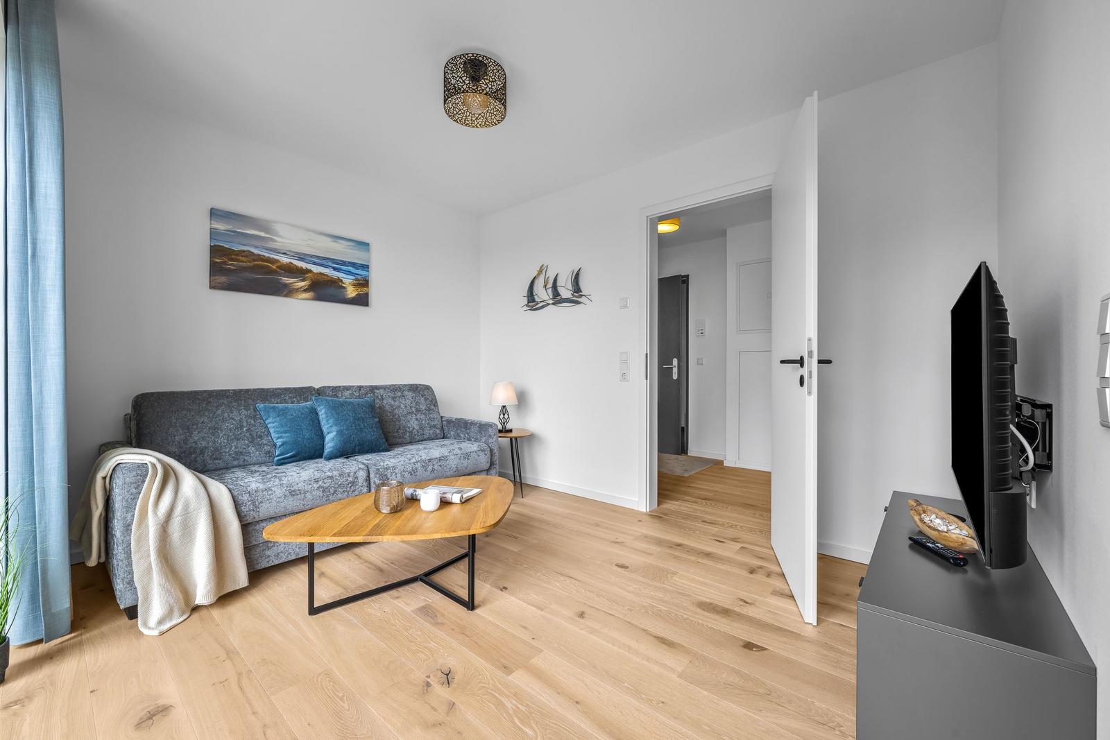 Wohnzimmer mit Sofa, Couchtisch und Fernseher. Holzboden und Wandbild mit Strandmotiv.