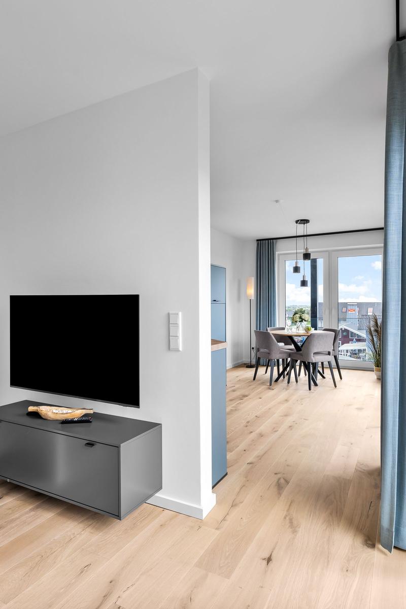 Wohn- und Essbereich mit TV, Holzboden und Blick auf die Dächer.