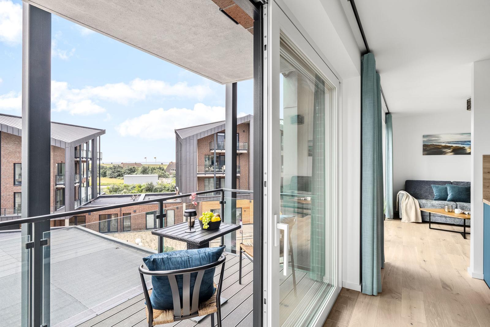 Terrasse mit Tisch und Stuhl. Durch Glastür zum Wohnzimmer mit Sofa und Holzboden.