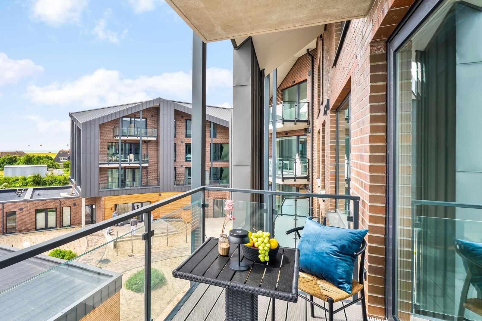 Terrasse mit Tisch, Stuhl und Kissen. Blick auf moderne Gebäude und Garten.