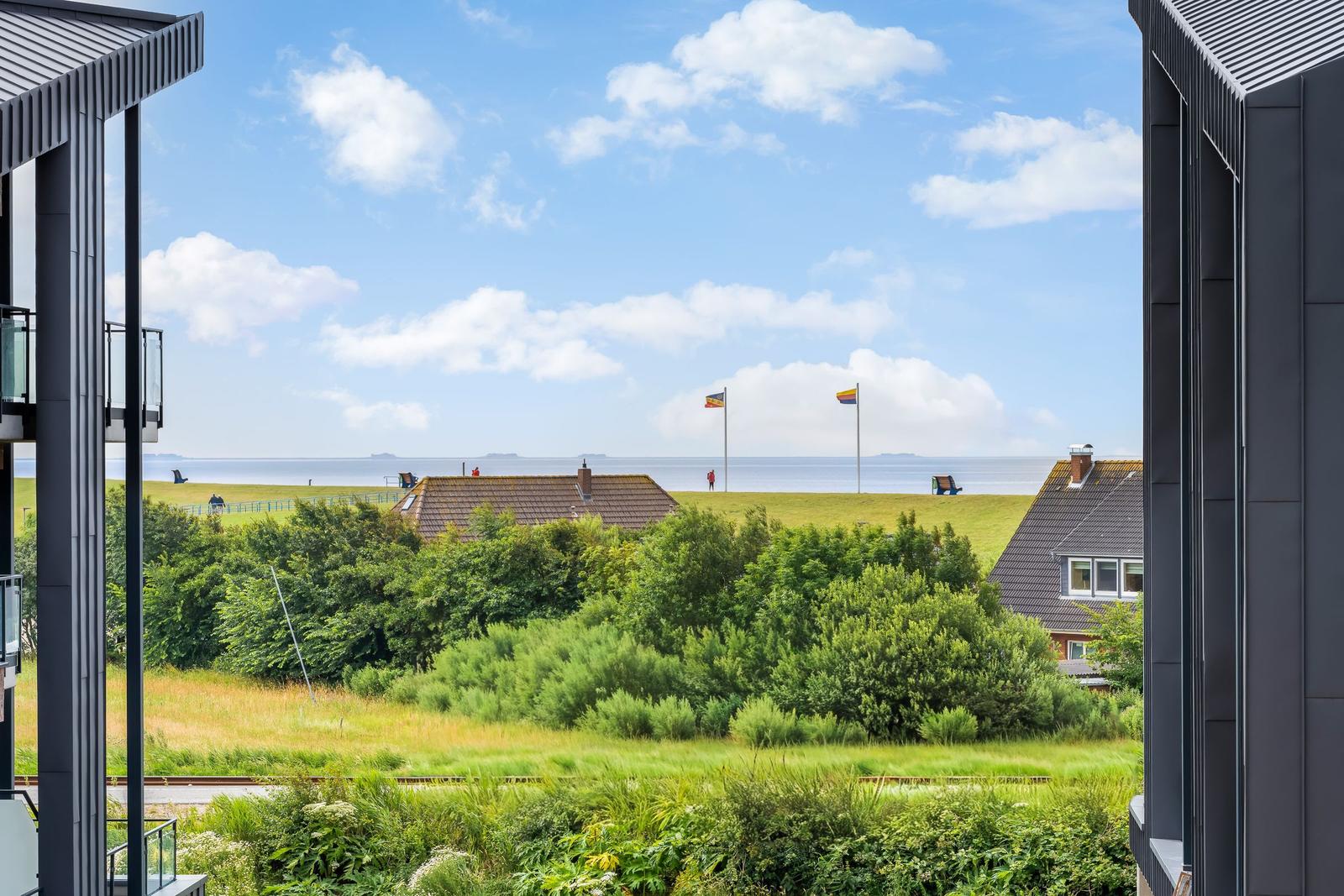 Ausblick auf grüne Wiesen, Häuser und Meer unter blauem Himmel mit weißen Wolken.
