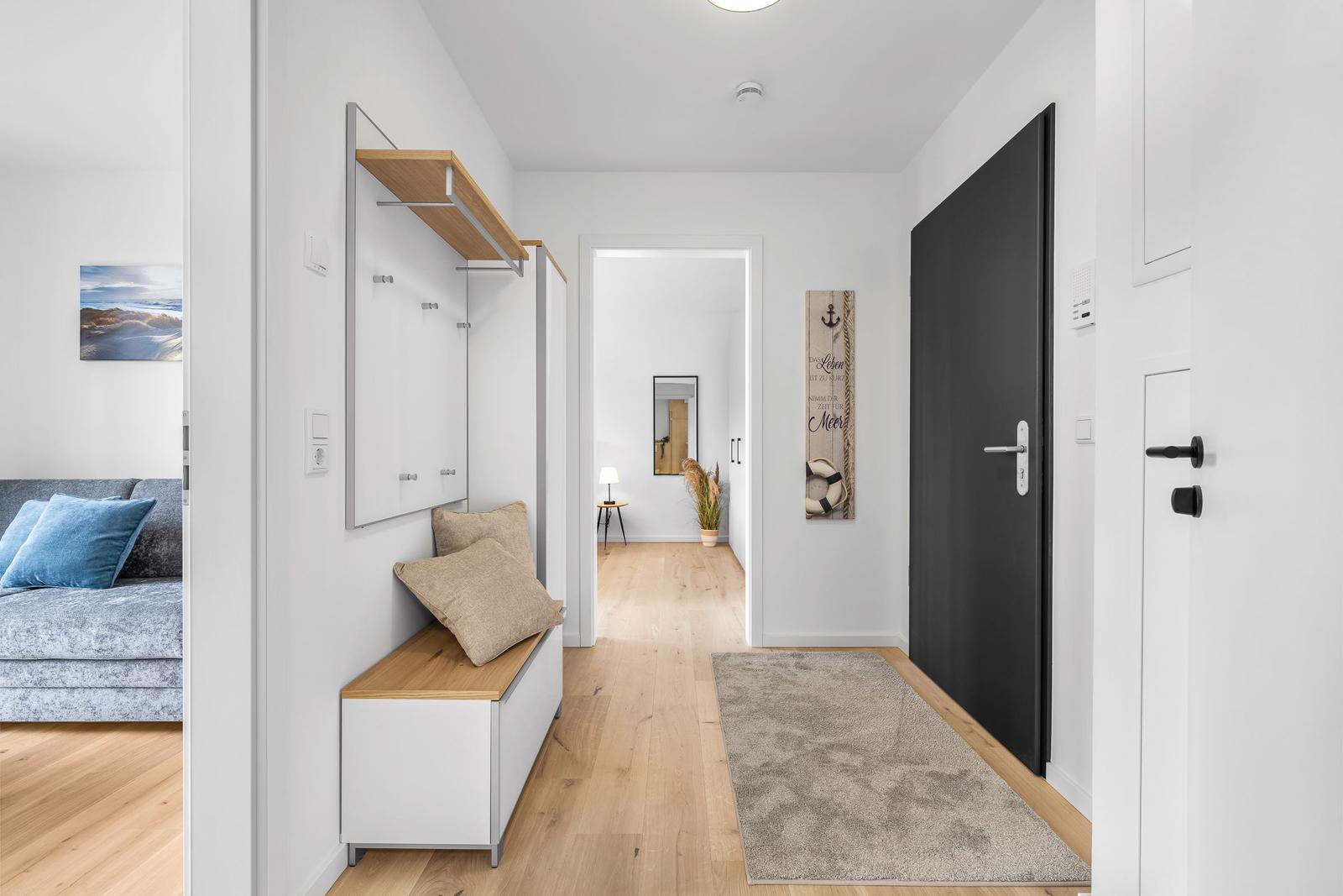 Hausflur mit Holzboden, Wandgarderobe und Teppich. Tür und Wohnzimmer sichtbar.