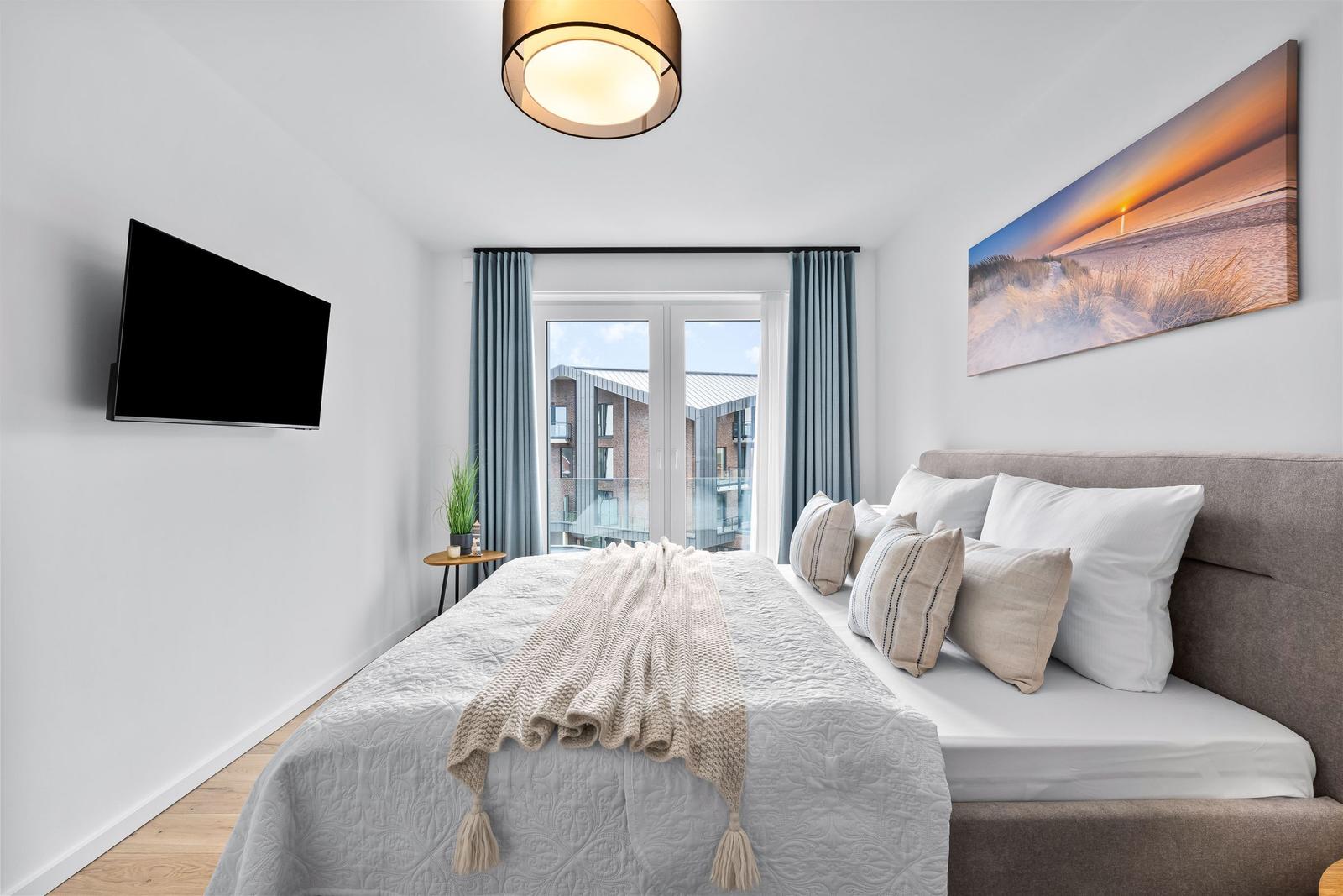 Schlafzimmer mit Bett, TV und Balkonansicht.