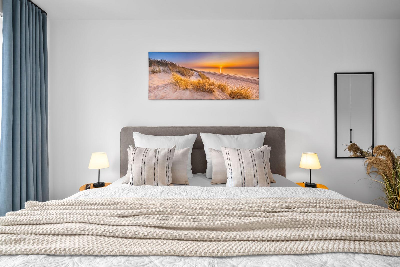 Schlafzimmer mit Bett, Nachttischen und Wandbild. Vorhänge und Spiegel sind sichtbar.