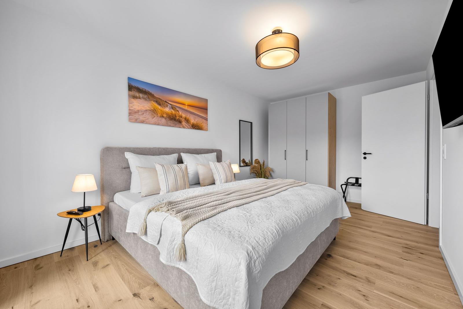 Schlafzimmer mit Bett, Nachttisch, Wandbild und Schrank.