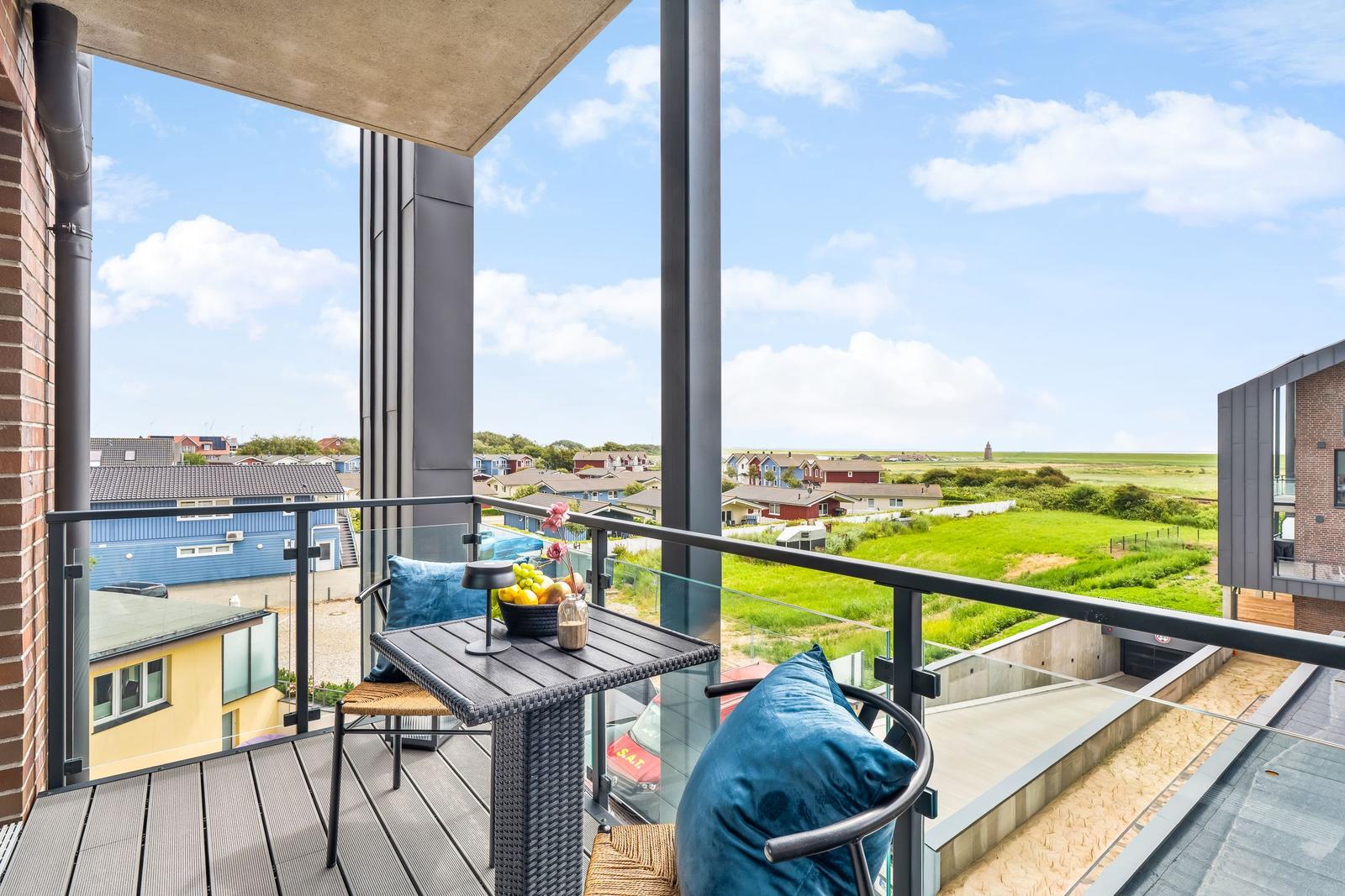 Terrasse mit Tisch, Stühlen und blauen Kissen. Blick auf grüne Landschaft und Häuser.