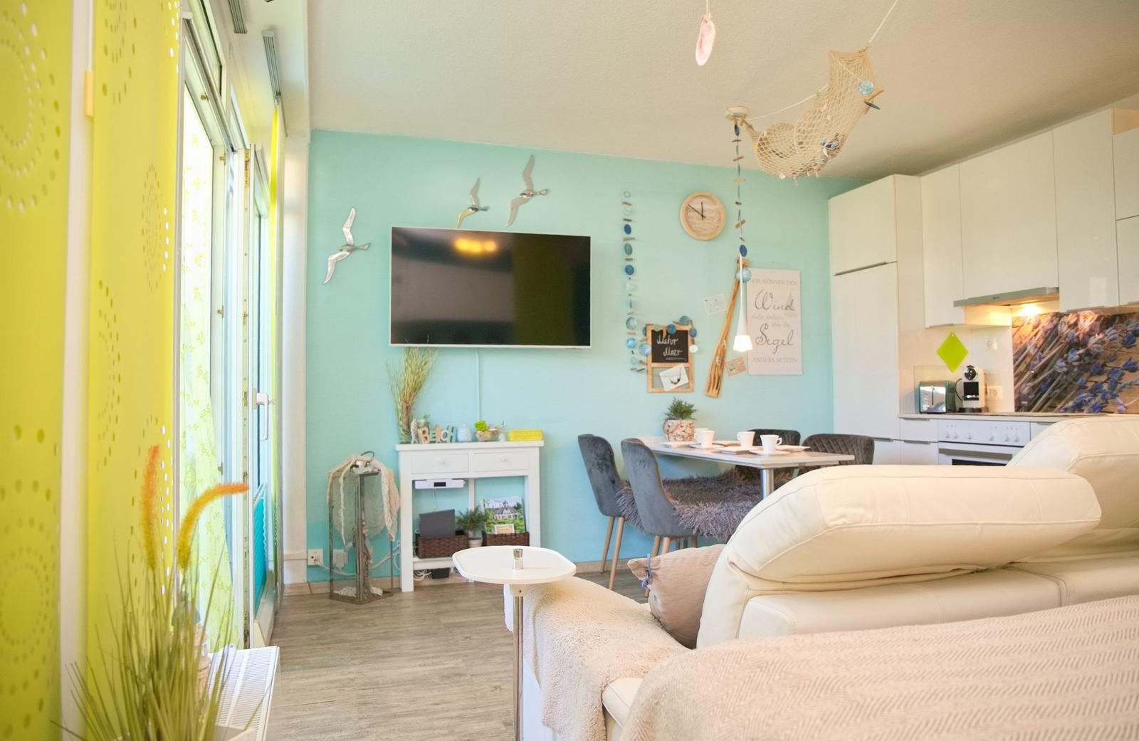 Wohnzimmer mit Essbereich und Küche. Wandfarbe mint, Sofa, Fernseher und Dekoration.