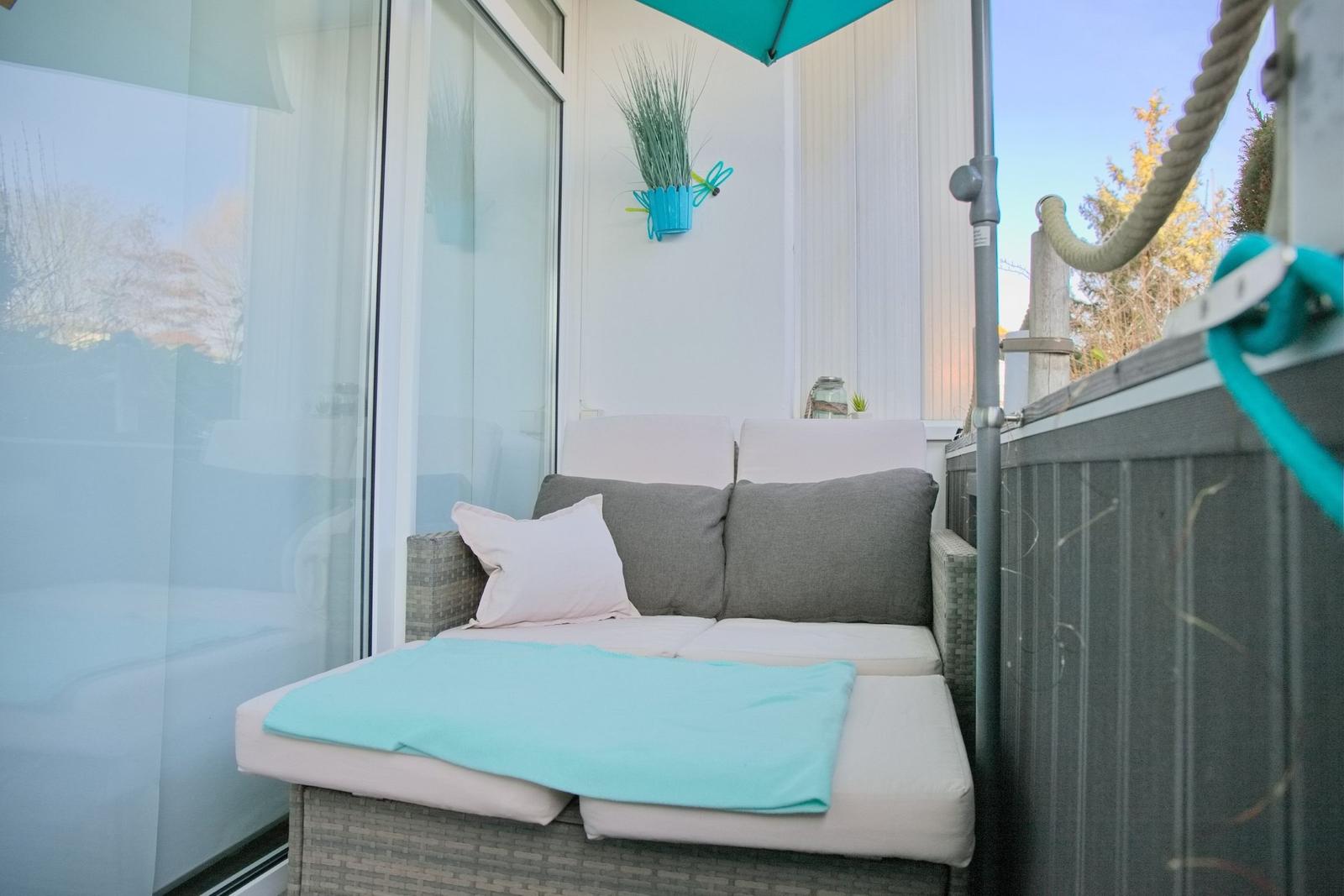 Terrasse mit Sitzbank, blauem Sonnenschirm und Pflanze an der Wand.