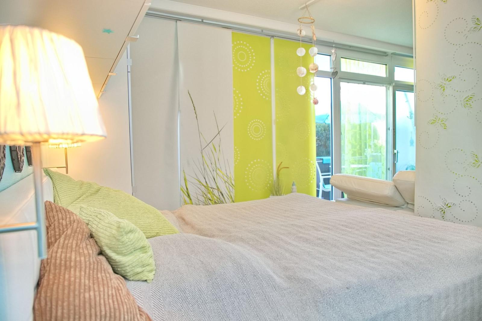 Schlafzimmer mit Bett, Lampe und Fenster zum Balkon