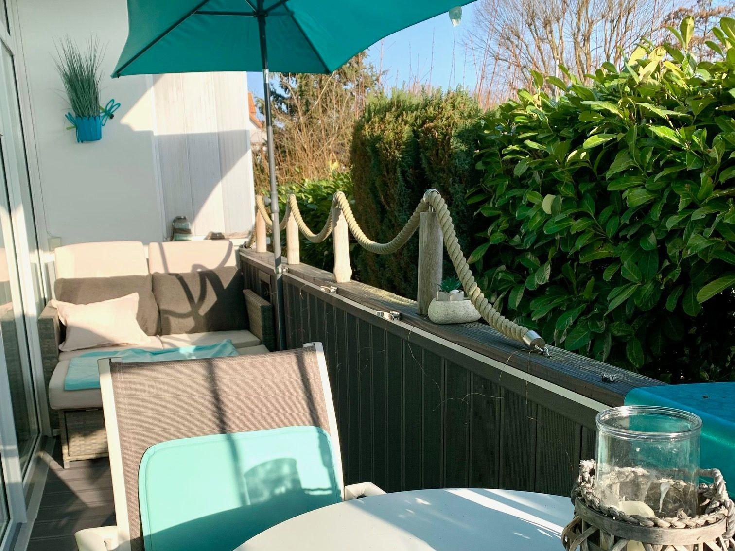 Terrasse mit Sitzgruppe, Sonnenschutz und Pflanzen. Holzgeländer und grüne Hecke umgeben den Außenbereich.