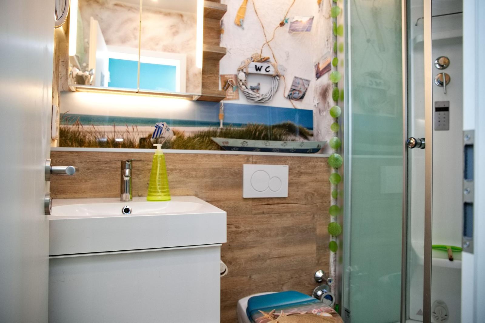 Badezimmer mit Waschbecken, Dusche und WC. Wanddekoration mit Strandmotiven.