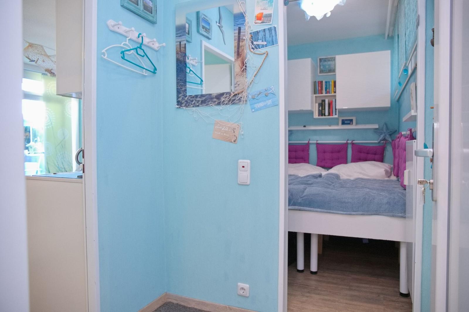Schlafzimmer mit Bett, Wandregalen und blauen Wänden. Haken und Spiegel an der Wand.