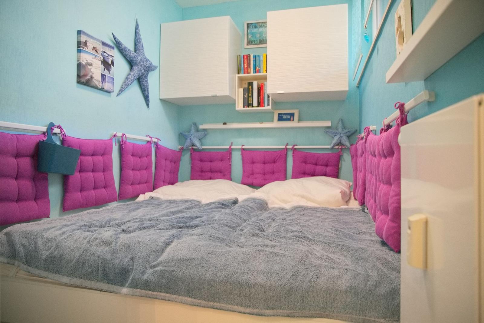 Schlafzimmer mit Bett, pinken Kissen und blauen Wänden mit Sternenbildern.