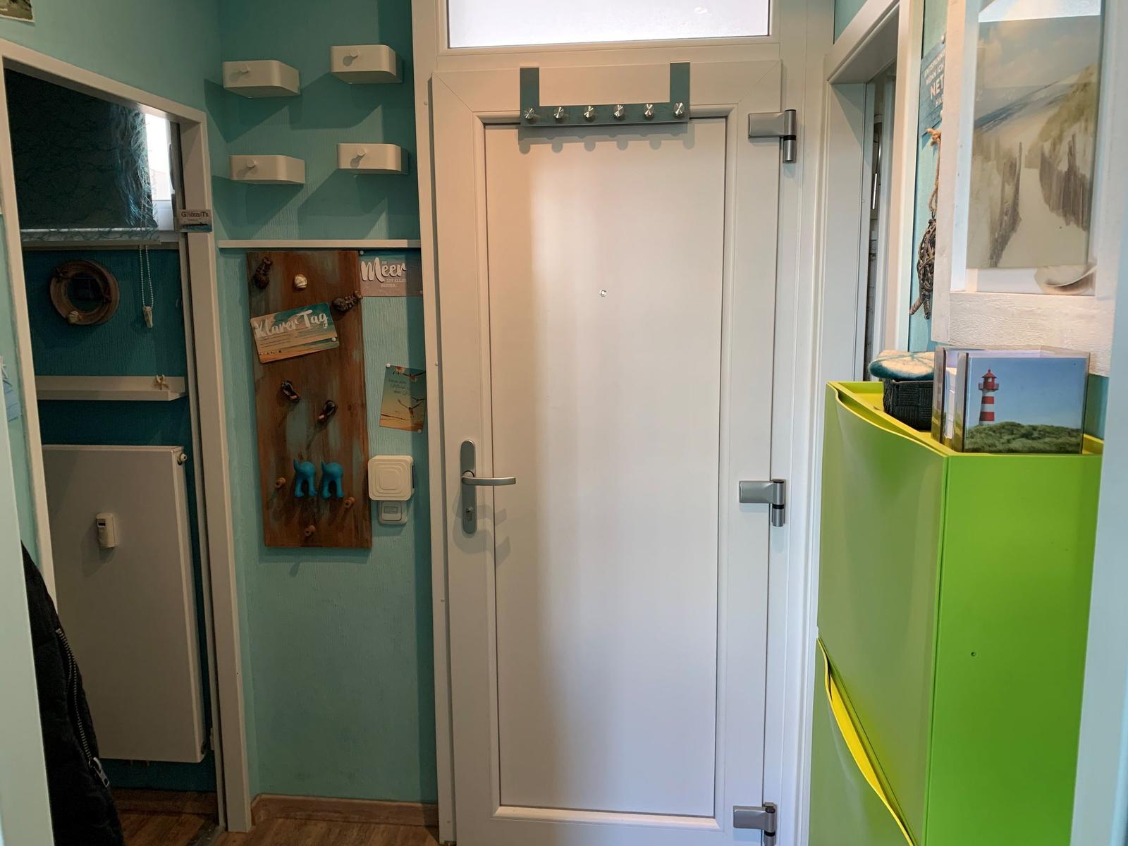 Eingangsbereich mit weißer Tür, hellblauer Wand und grünem Schrank.