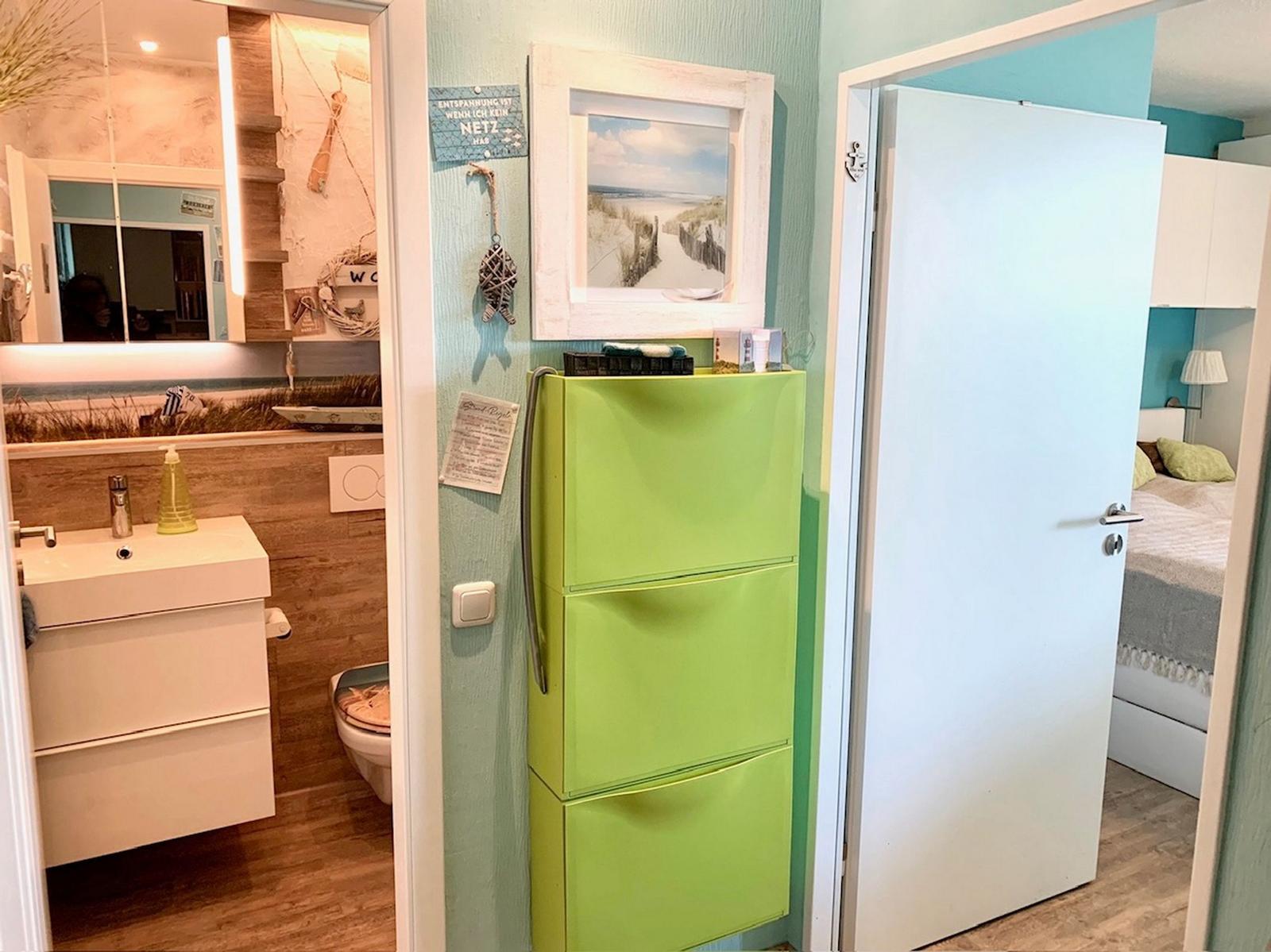 Badezimmer mit Waschbecken und Toilette. Grüner Schrank und Schlafzimmer mit Bett.