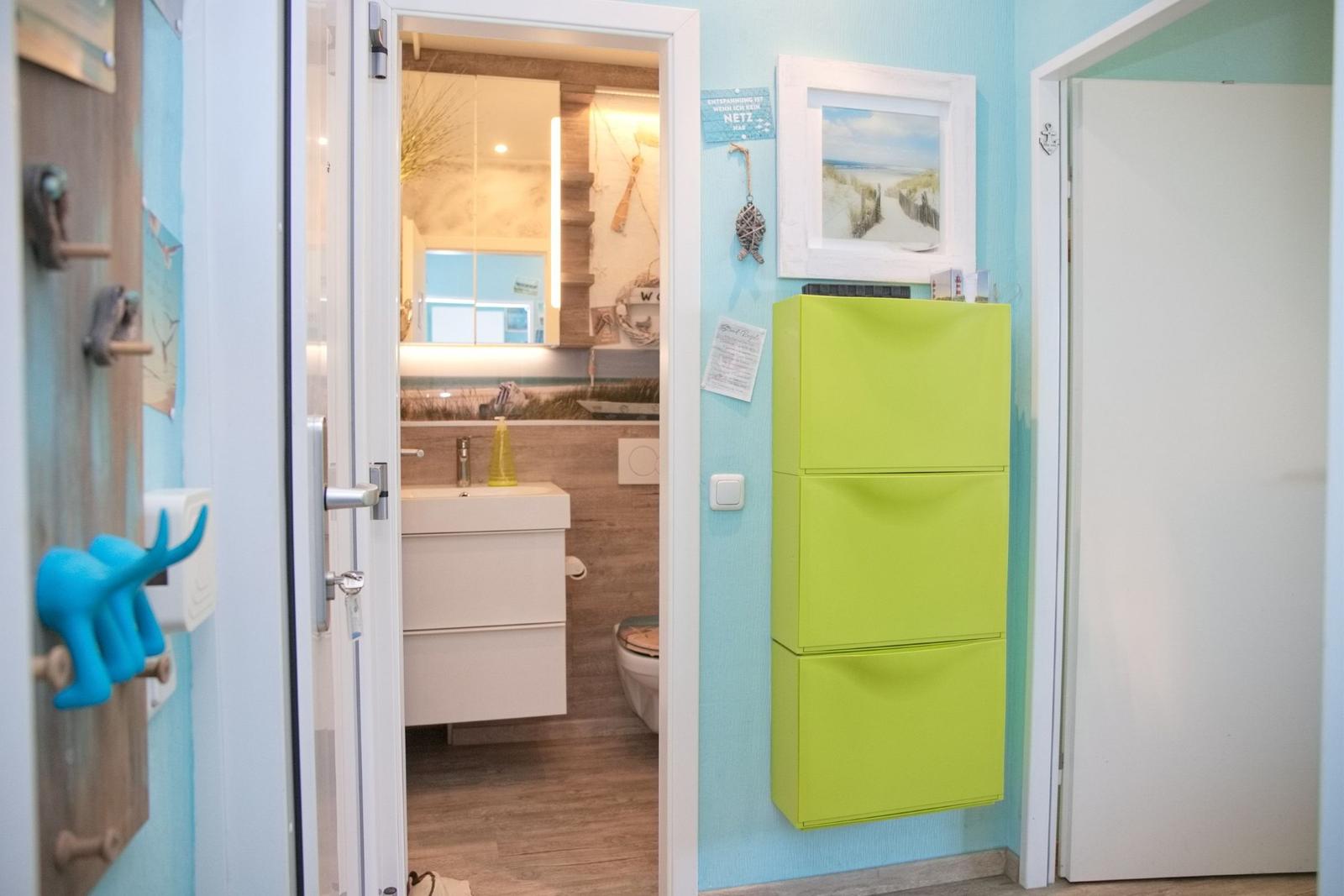 Badezimmer mit Waschbecken und Toilette, Wandregal und Strandmotiv an der Wand.