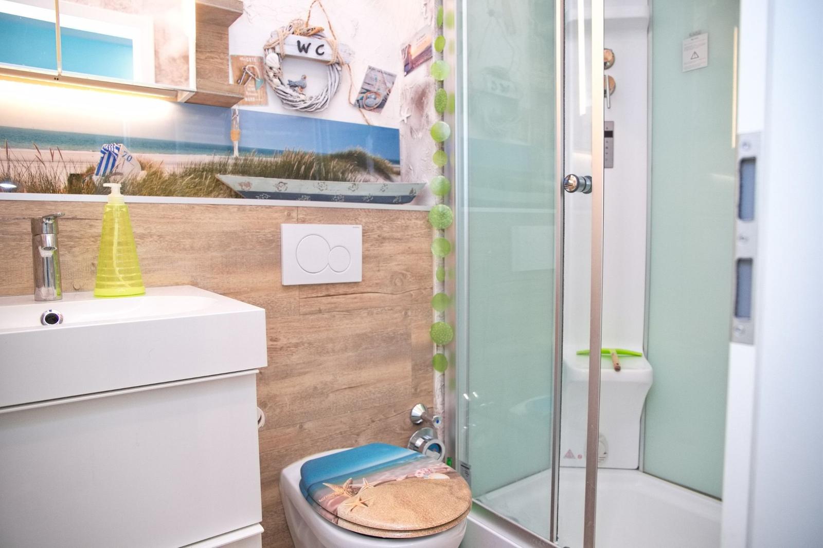 Badezimmer mit Dusche, Toilette und Waschbecken. Wandbild und Dekoration im Strandstil.