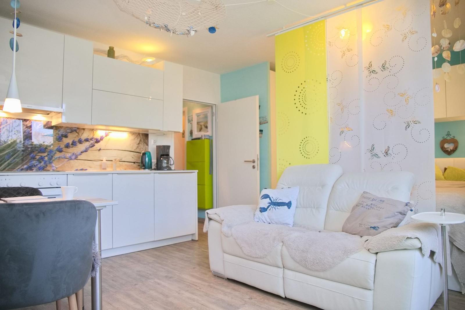 Wohnküche mit weißem Sofa, Küchenzeile und farbigen Wänden.