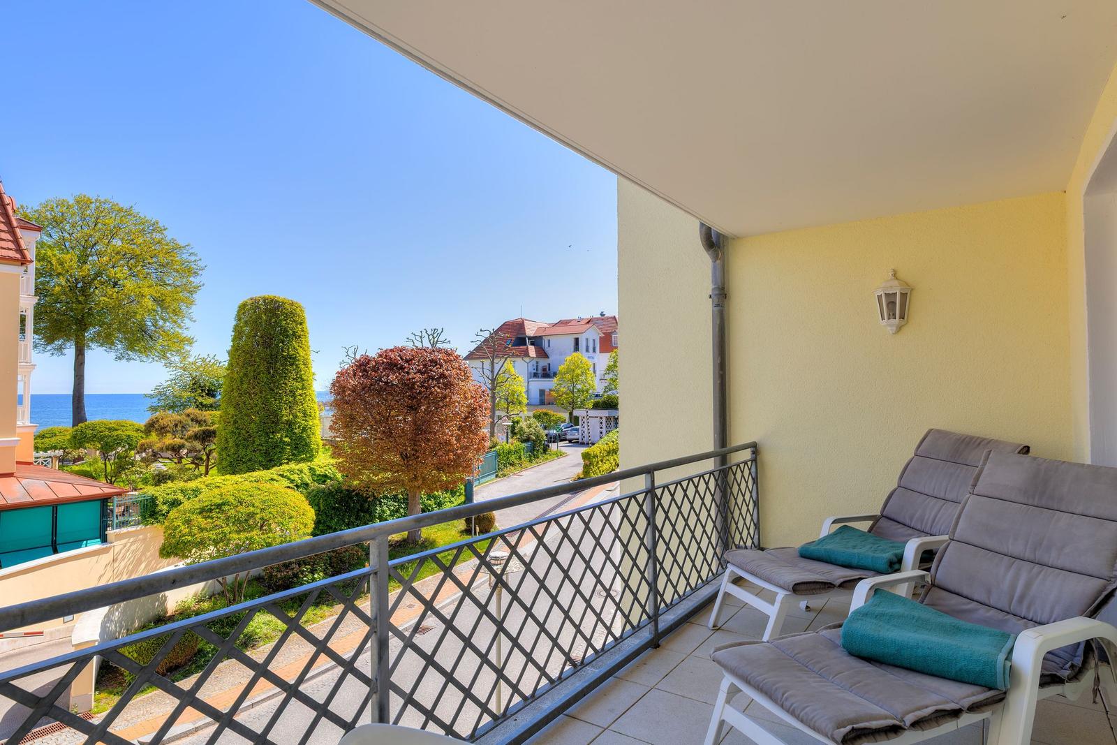 Terrasse mit Liegestühlen und Meerblick durch grüne Bäume und Sträucher.