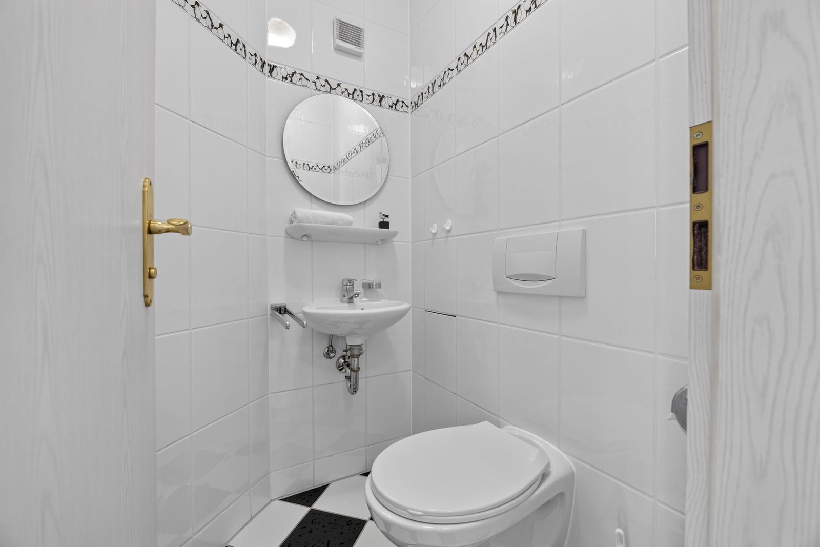 Badezimmer mit Toilette, Waschbecken und Spiegel an weißen Wänden.