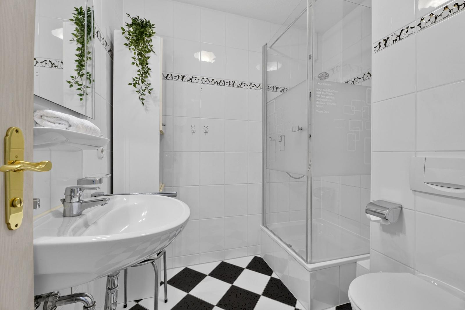 Badezimmer mit Dusche, Waschbecken und Toilette. Schwarze und weiße Fliesen.