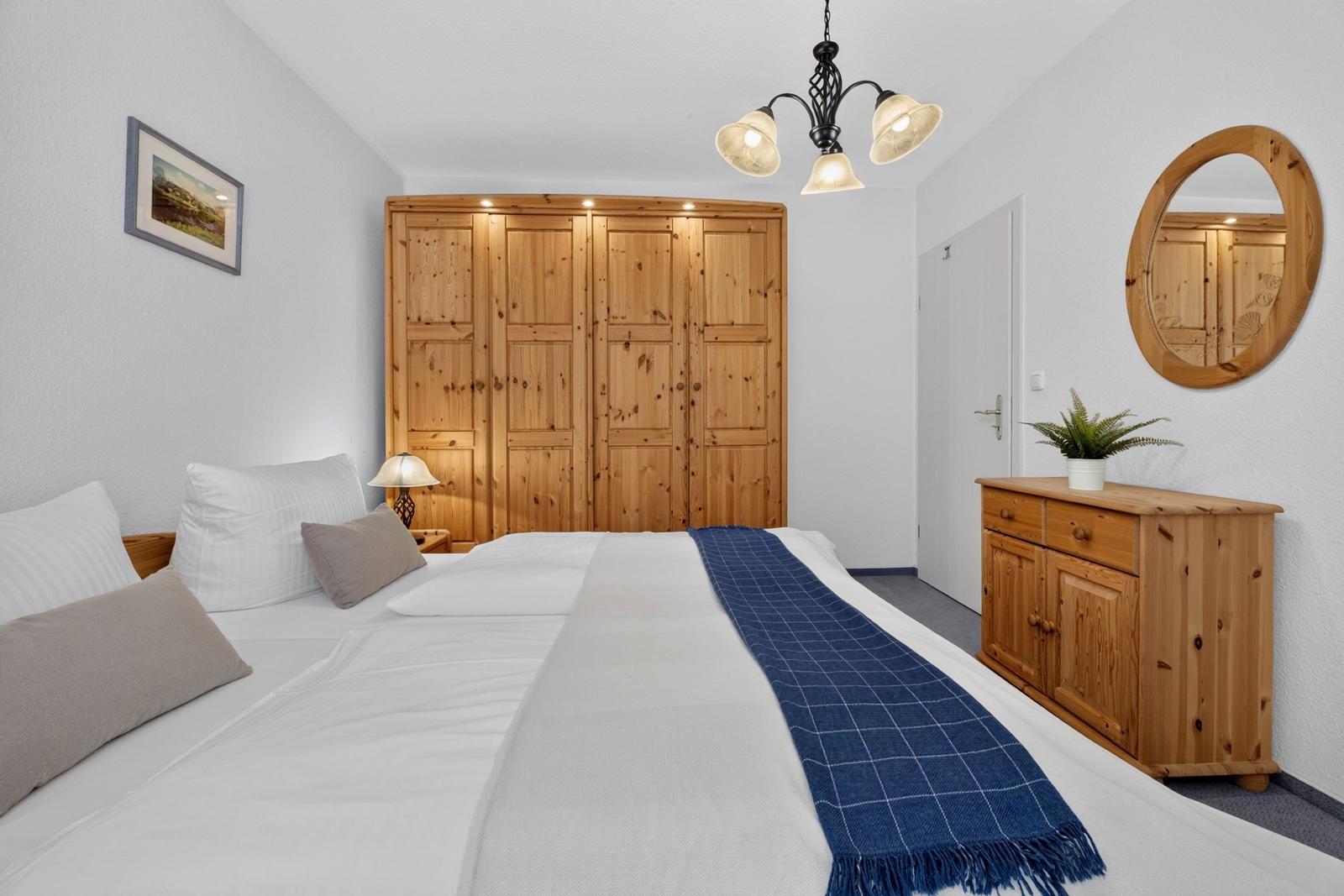 Schlafzimmer mit Holzschrank, Bett und Schminktisch mit Spiegel.