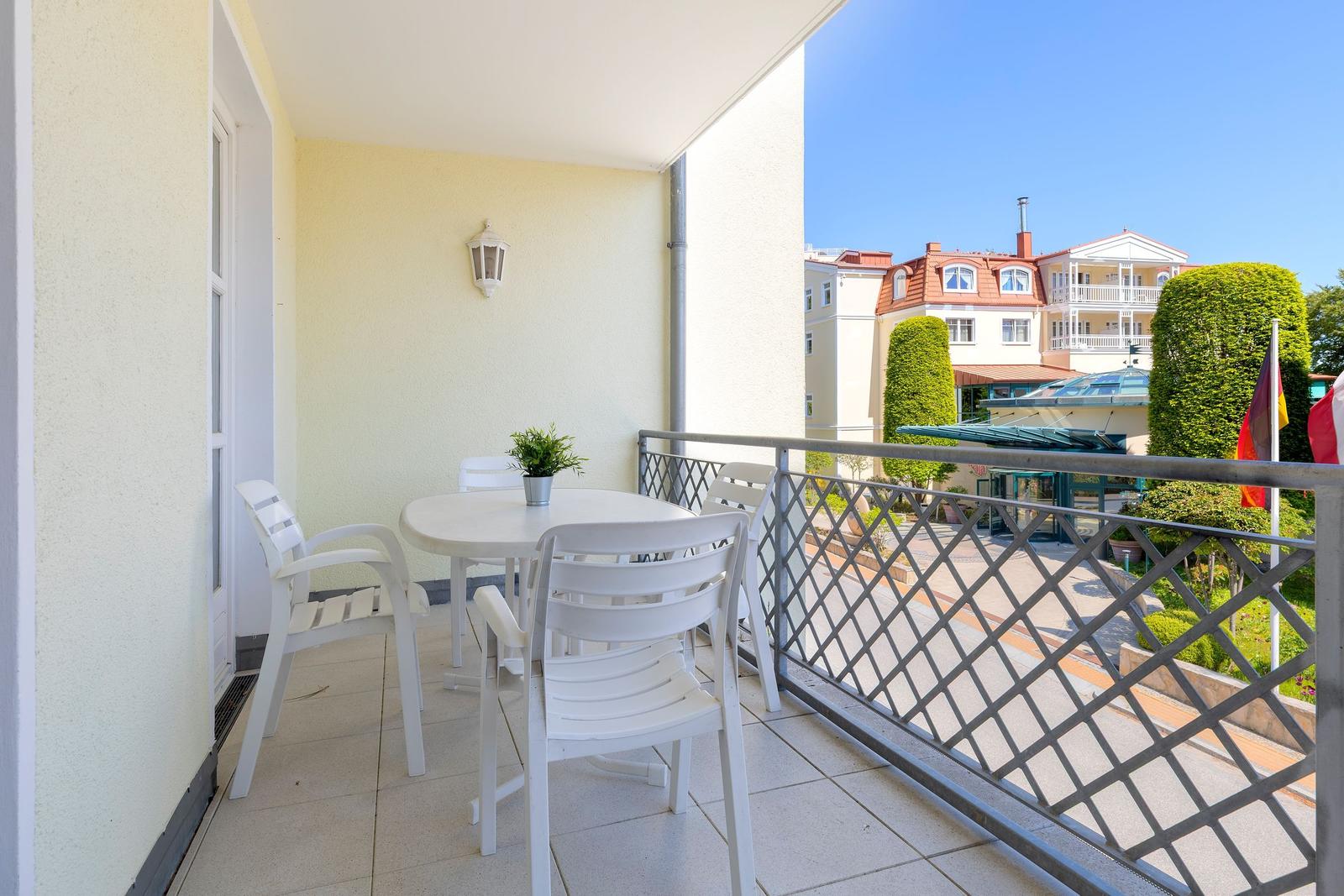 Terrasse mit weißem Tisch und Stühlen, Blick auf Gebäude und Bäume.