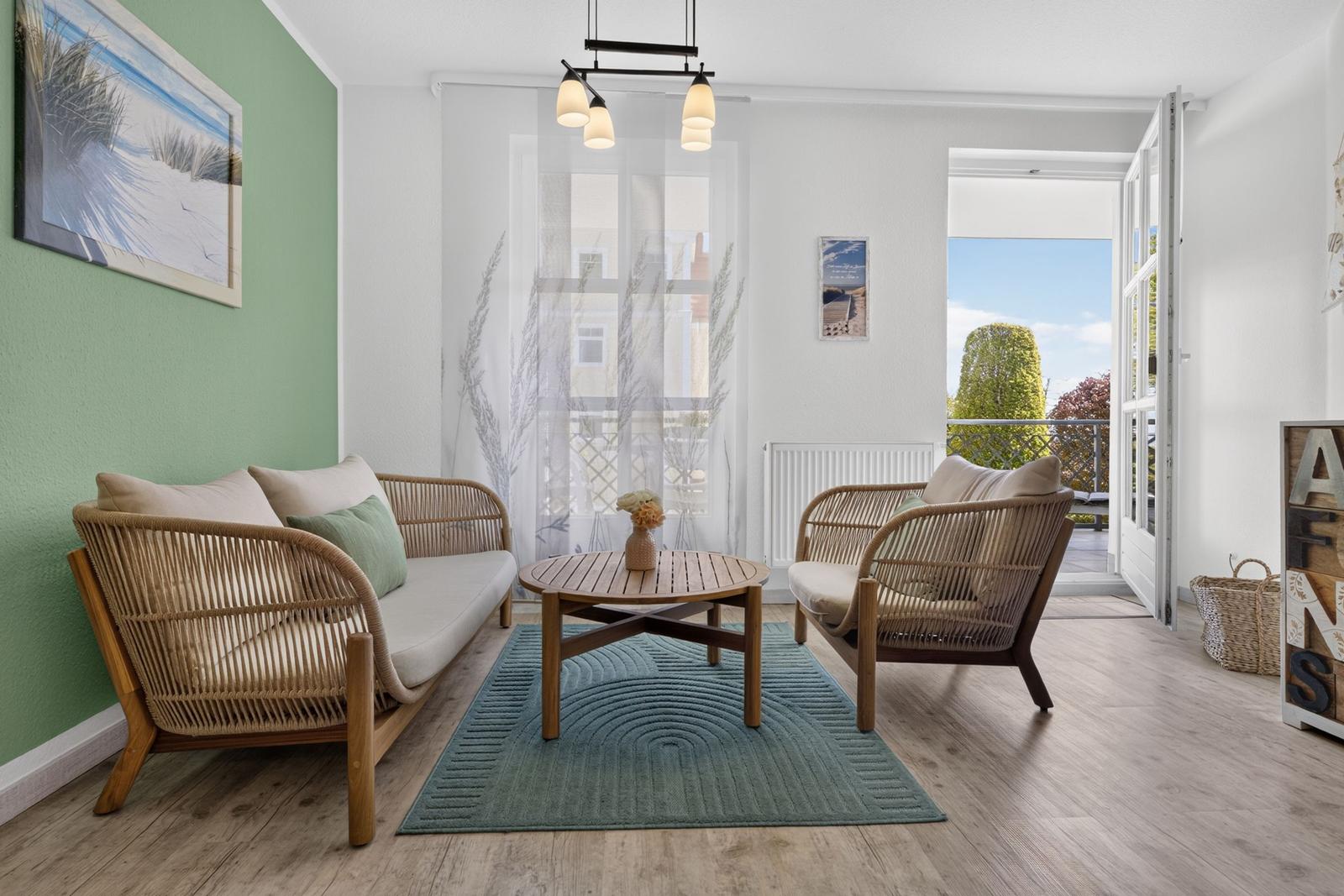 Wohnzimmer mit Sofa, Sessel und Tisch. Durchgang zur Terrasse. Wandbild und Teppich.