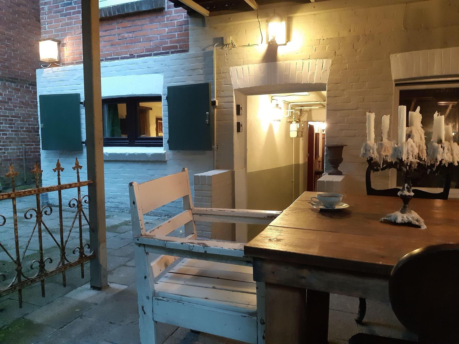 Helle Terrasse mit Holztisch, Stuhl und Kerzenständer. Weiße Mauern und Gittertor im Hintergrund.