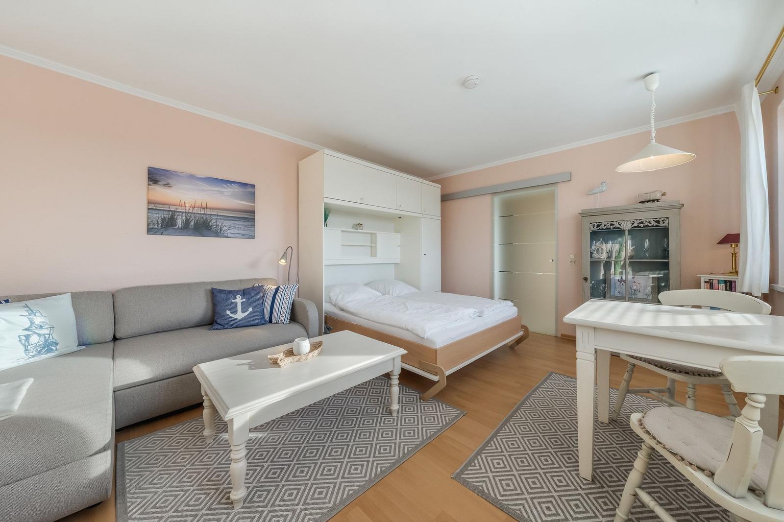 Living area with sofa, bed, and dining table. Wall art shows beach.