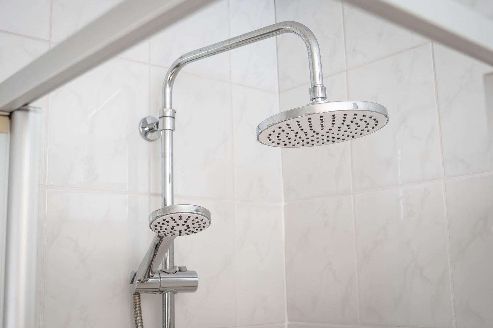 Shower head with handheld shower and chrome fixture on white tiles.