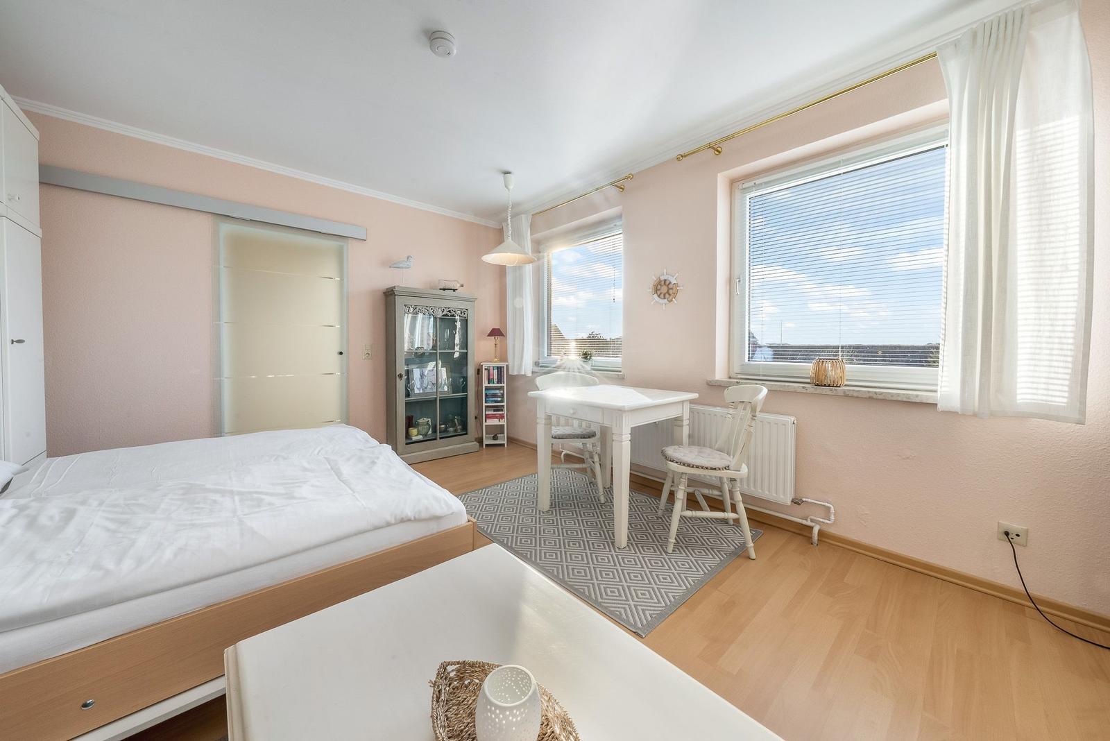 Bedroom with bed, desk, and windows. Wooden floor and pink walls.