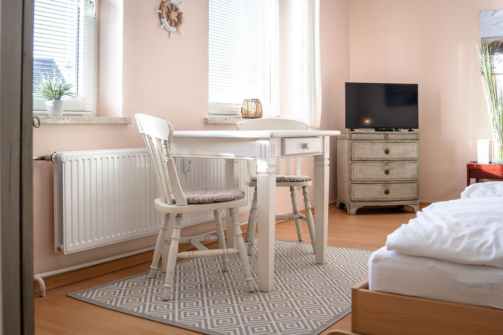 A bedroom with a white desk, chairs, TV, and bed.