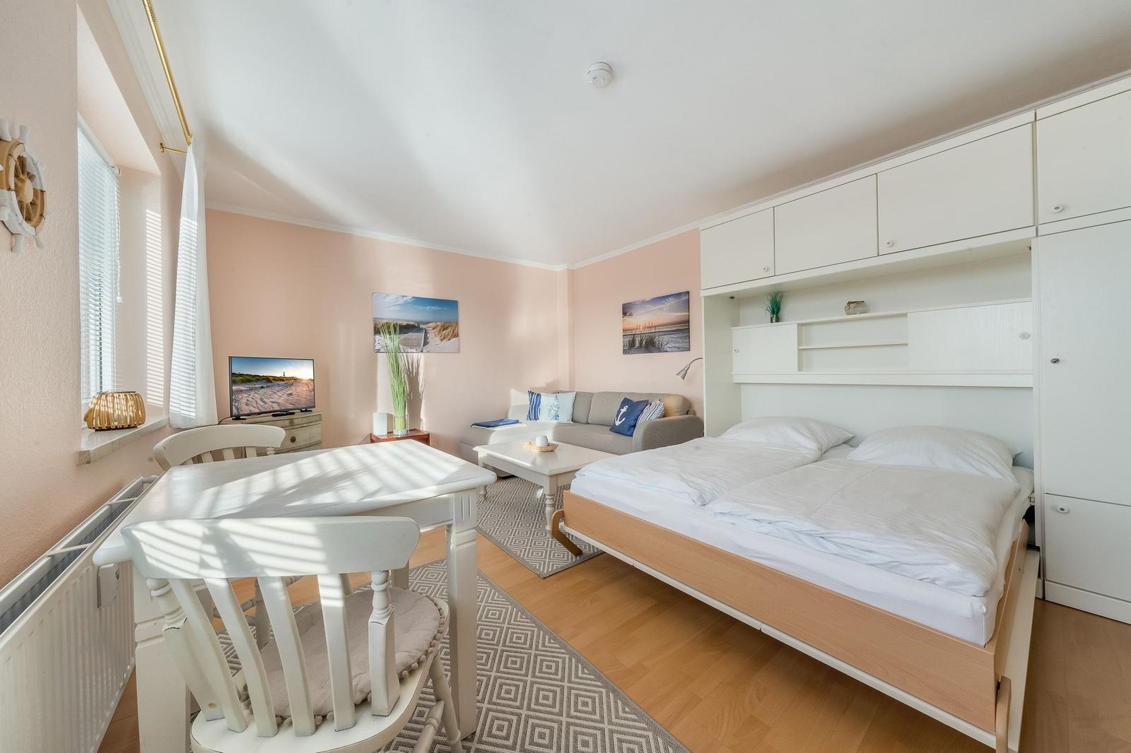 Bedroom with double bed, sofa, dining table, and wall pictures.