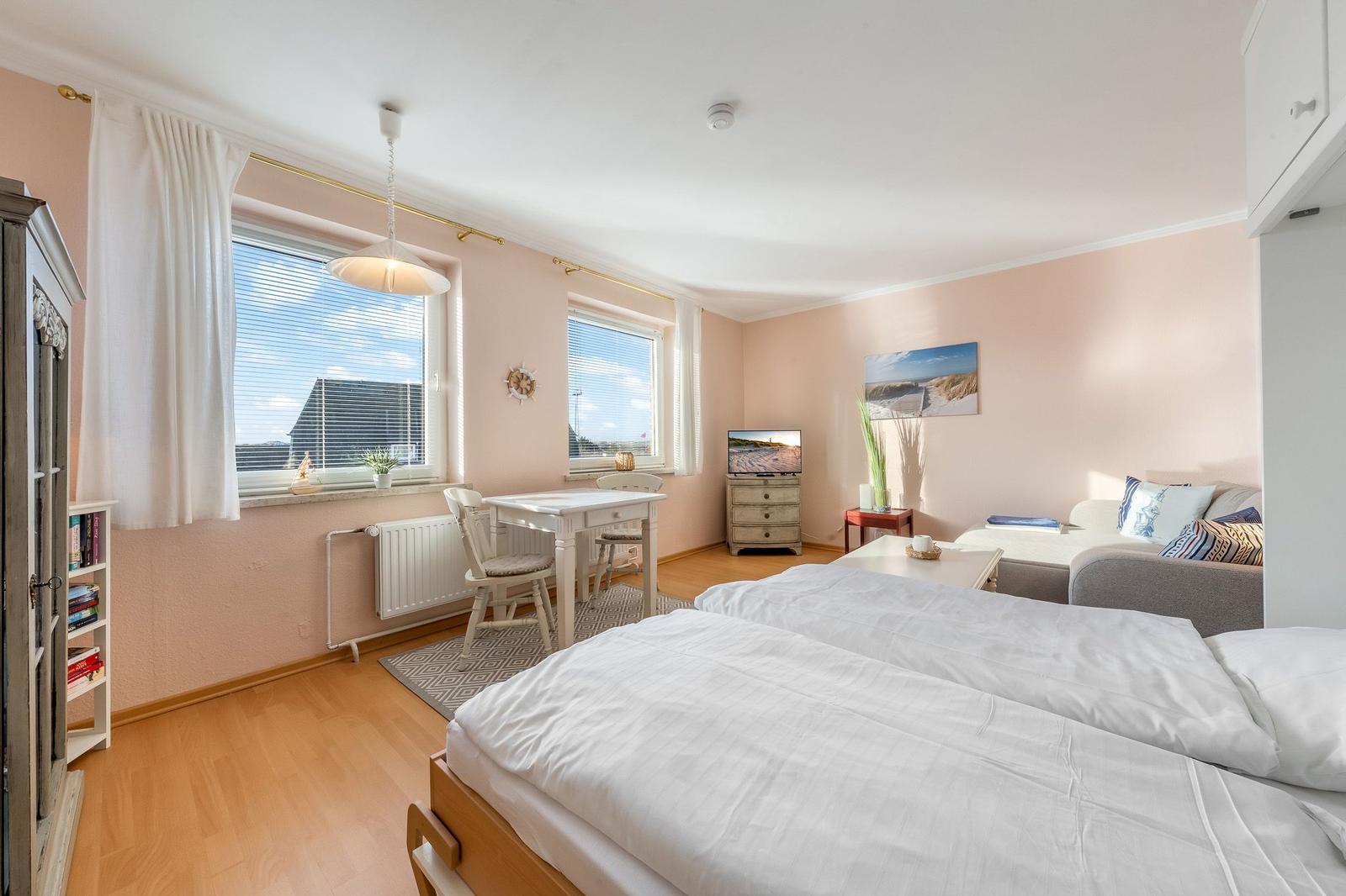 Two beds, sofa, table, and windows with view. Wall art and wardrobe.