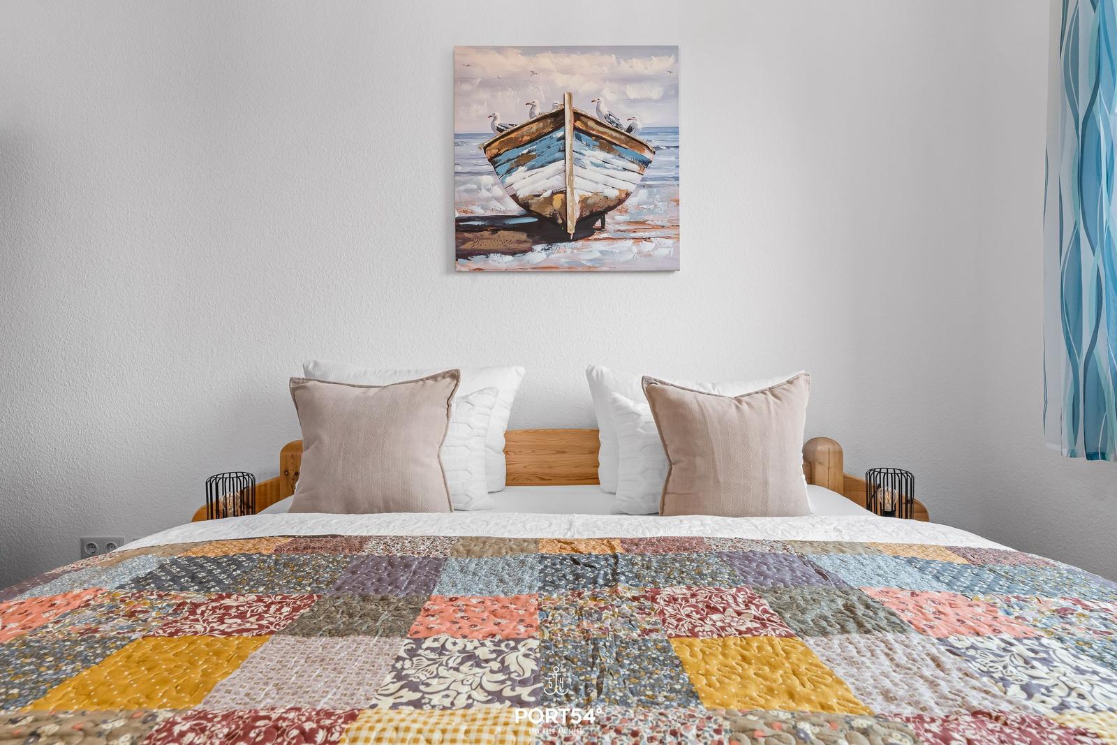 Das Bett mit buntem Quilt und Wandbild eines Boots.
