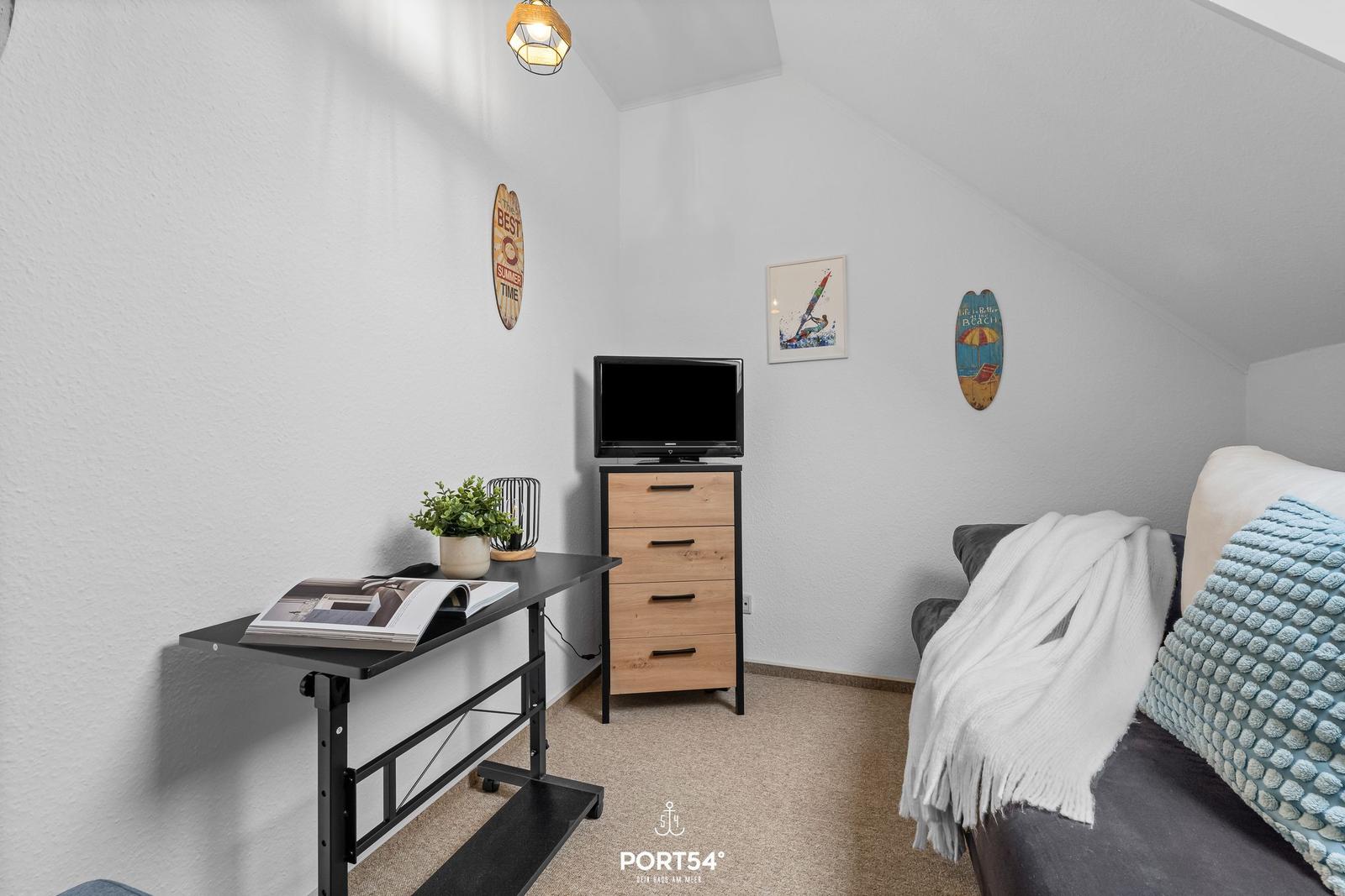 Schlafzimmer mit TV, Schreibtisch und Sofa unter Dachschrägen.